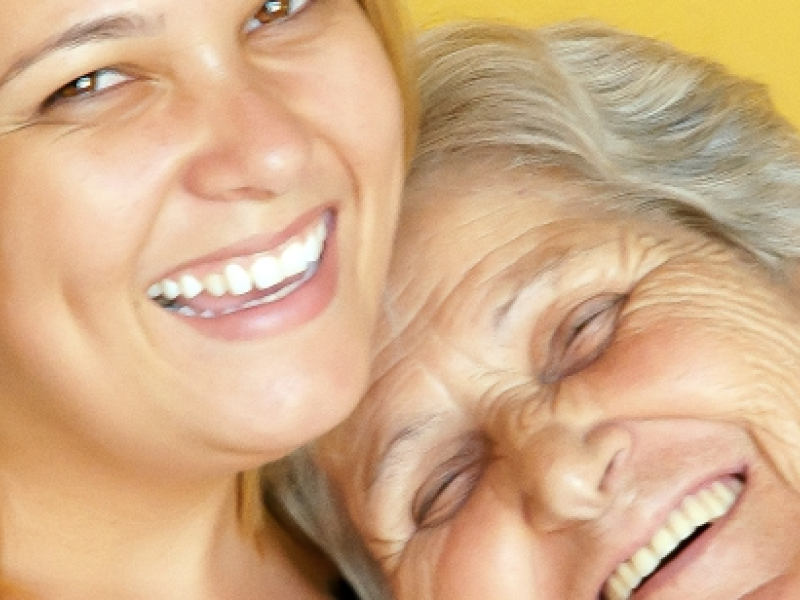 Older woman smiling with shoulder on younger woman smiling