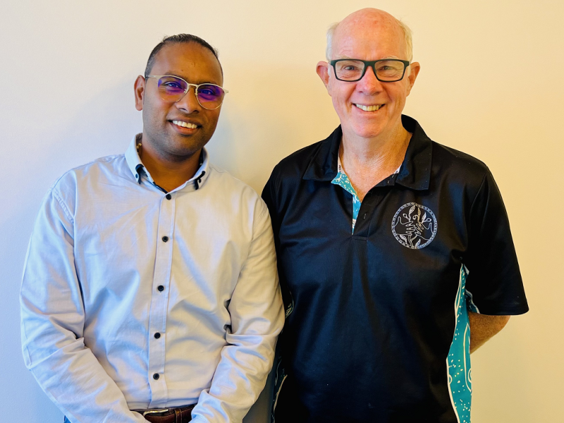 Two men standing against a wall smiling