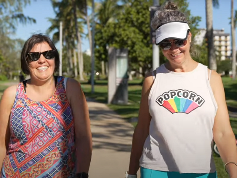 Two women smiling and walking through a park in summer