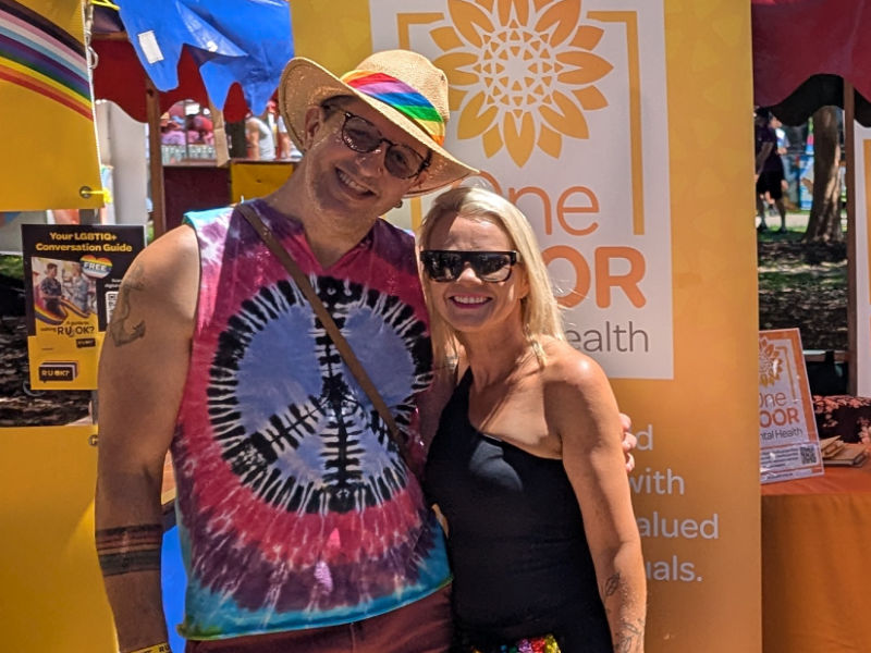Two people standing in front of a banner at Mardi Gras