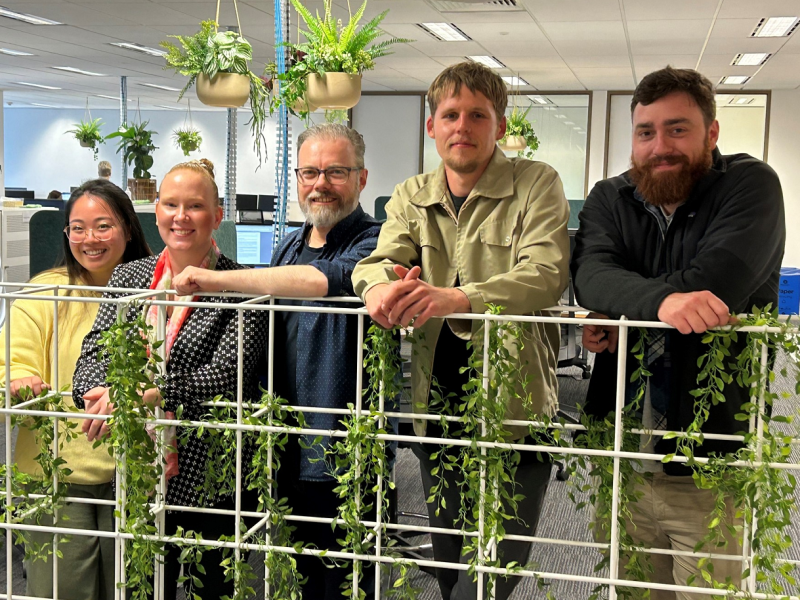 Three men and two women smiling for a group photo in an office